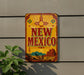 A vintage-style metal sign with the text "NEW MEXICO" displayed prominently, featuring a desert landscape and a sun motif.