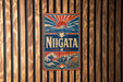 A vintage-style metal sign with the word "NIGATA" prominently displayed, featuring a sun and mountain landscape design.