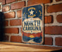 A vintage metal sign with the text "NORTH CAROLINA" and a star, hanging on a brick wall.