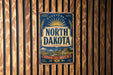 A vintage metal sign with the text "NORTH DAKOTA" and a sun-like symbol is displayed on a wooden wall.