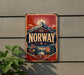 a vintage-style metal sign with the word "NORWAY" prominently displayed, along with a mountain landscape and sailing ships, all set against a red and blue background.