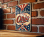 A vintage-style metal sign with the word "Ohio" prominently displayed, featuring a city skyline and stars in the background.