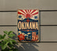 a vintage-style sign with the name "OKINAWA" prominently displayed, surrounded by various decorative elements such as a sun, palm trees, and a lion.
