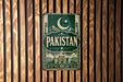 A vintage metal sign with the word "PAKISTAN" displayed prominently in the center, surrounded by a decorative border and a crescent moon and star symbol.