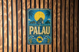 A vintage-style metal sign with a tropical island landscape and palm trees, featuring the word "PALAU" prominently displayed.