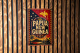 A vintage metal sign with the text "PAPUA NEW GUINEA" displayed prominently, featuring a bird and tropical landscape.