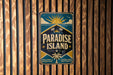 A vintage-style metal sign with the text "Paradise Island" displayed prominently in the center, surrounded by tropical elements such as palm trees and a sun.