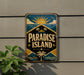 A vintage-style sign for "Paradise Island" is displayed on a wall, featuring a sun, palm trees, and a tropical landscape.