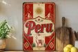 a vintage-style metal sign with the word "Peru" prominently displayed, surrounded by decorative elements such as a sun, mountains, and a llama. The sign is placed on a shelf next to a wooden cutting board and a potted plant, creating a rustic and charming atmosphere.