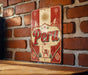 A vintage-style metal sign with the word "Peru" prominently displayed, mounted on a brick wall.