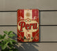 a vintage-style sign with the word "Peru" prominently displayed in the center. The sign is mounted on a wall, and there is a plant visible to the left of the sign.