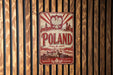 A vintage metal sign with the word "POLAND" prominently displayed, featuring a red and white color scheme and a stylized illustration of a Polish castle.