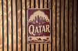 a vintage-style sign with the word "Qatar" prominently displayed, mounted on a wooden wall.