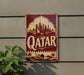 a vintage-style sign with the word "Qatar" prominently displayed, along with a desert landscape and a camel.