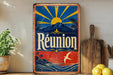 A vintage-style metal sign with a tropical landscape and sun design, featuring the word "Reunion" prominently displayed.