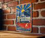 A vintage metal sign with a sun and palm tree design hangs on a brick wall.