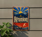 A vintage-style sign for Reunion beer, featuring a sun and palm trees, is displayed on a wall next to a plant.