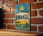 A vintage-style metal sign with the word " RWANDA" prominently displayed, featuring a sun and mountain landscape.