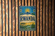 a vintage-style sign with the word " RWANDA" prominently displayed, set against a wooden background with vertical slats.