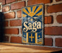 A vintage-style metal sign with a sun and mountain design, mounted on a brick wall.