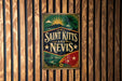 A vintage-style sign with the text "SAINT KITT'S AND NEVIS" displayed on a wooden wall.