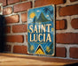 A vintage-style sign for Saint Lucia, featuring a tropical landscape with palm trees and mountains, is displayed on a brick wall.