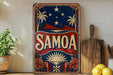 a vintage-style sign with the word "SAMOA" prominently displayed, surrounded by a tropical landscape with palm trees and a starry night sky. The sign is placed on a shelf next to a wooden cutting board and a potted plant, creating a visually appealing and decorative display.