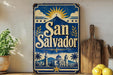 A vintage-style sign for San Salvador, featuring a blue background with a sun and mountains, and the text "San Salvador" prominently displayed.