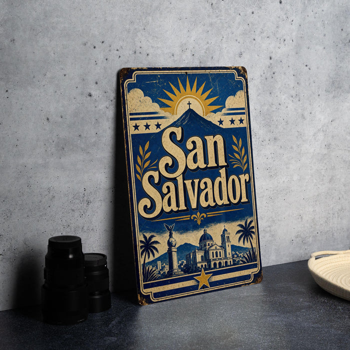 A vintage-style metal sign with the text "San Salvador" prominently displayed, featuring a sun and palm trees, is placed on a gray surface next to some black camera lenses.