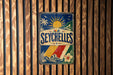 A vintage metal sign with a tropical design hangs on a wooden wall.