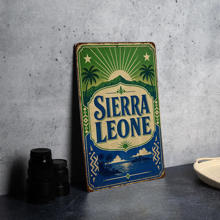 A vintage-style sign for Sierra Leone, featuring palm trees, mountains, and a sunburst design, is displayed on a gray countertop next to a stack of black camera lenses.