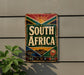 A vintage-style sign with the text "SOUTH AFRICA" displayed prominently, featuring a sun and floral design.