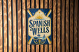 A vintage-style sign for "Spanish Wells" is displayed on a wooden wall.