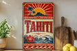 A vintage-style sign for Tahiti, featuring a tropical landscape with palm trees, a sun, and a mountain.