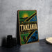 A vintage-style metal sign with the word "TANZANIA" prominently displayed, featuring a sun, mountain, and other African-inspired elements.