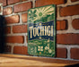 A vintage-style sign with the word "Tochigi" displayed prominently, featuring a sun, mountains, and a bridge. The sign is mounted on a brick wall, and there is a wooden table in the foreground.