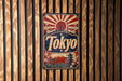 A vintage-style metal sign with the word "Tokyo" prominently displayed, featuring a sun and Japanese-style architecture.