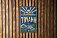 A vintage-style metal sign with the word "TOYAMA" prominently displayed, featuring a mountain landscape and a wave-like design.