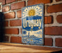 A vintage-style metal sign with the word "Uruguay" prominently displayed, featuring a sun and palm trees, against a brick wall background.