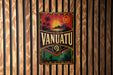 A vintage metal sign with the word "VANUATU" prominently displayed, featuring a tropical landscape with palm trees, mountains, and a sun.