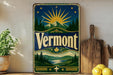 A vintage-style metal sign with a sunburst design and mountains in the background, featuring the word "Vermont" prominently displayed.