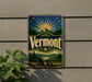 A vintage Vermont beer sign is displayed on a wall, featuring a sunburst design with mountains, pine trees, and a river.