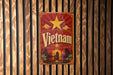 A vintage-style metal sign with the word "Vietnam" prominently displayed, featuring a red background with a yellow star and a landscape scene.
