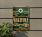 A vintage metal sign with the text "Wakayama" displayed prominently, featuring a scenic landscape with mountains, clouds, and a sun.