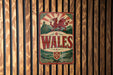 A metal sign with a red dragon and the word "WALES" in the center, mounted on a wooden wall.