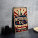 A vintage-style metal sign with the text "WASHINGTON DC" prominently displayed, featuring a stylized depiction of the United States Capitol building and the Washington Monument.