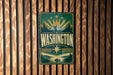 A vintage-style metal sign with the word "WASHINGTON" prominently displayed, featuring a mountain landscape and sunburst design.