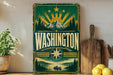 A vintage-style metal sign with the word "WASHINGTON" prominently displayed, featuring a mountain landscape and sunburst design.