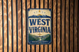 A vintage-style metal sign with the text "WEST VIRGINIA" and a mountain landscape, mounted on a wooden wall.