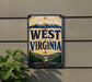 A vintage-style sign for West Virginia, featuring mountains, a bridge, and the text "MOUNTAIN STATE" against a blue background with a sun and stars.